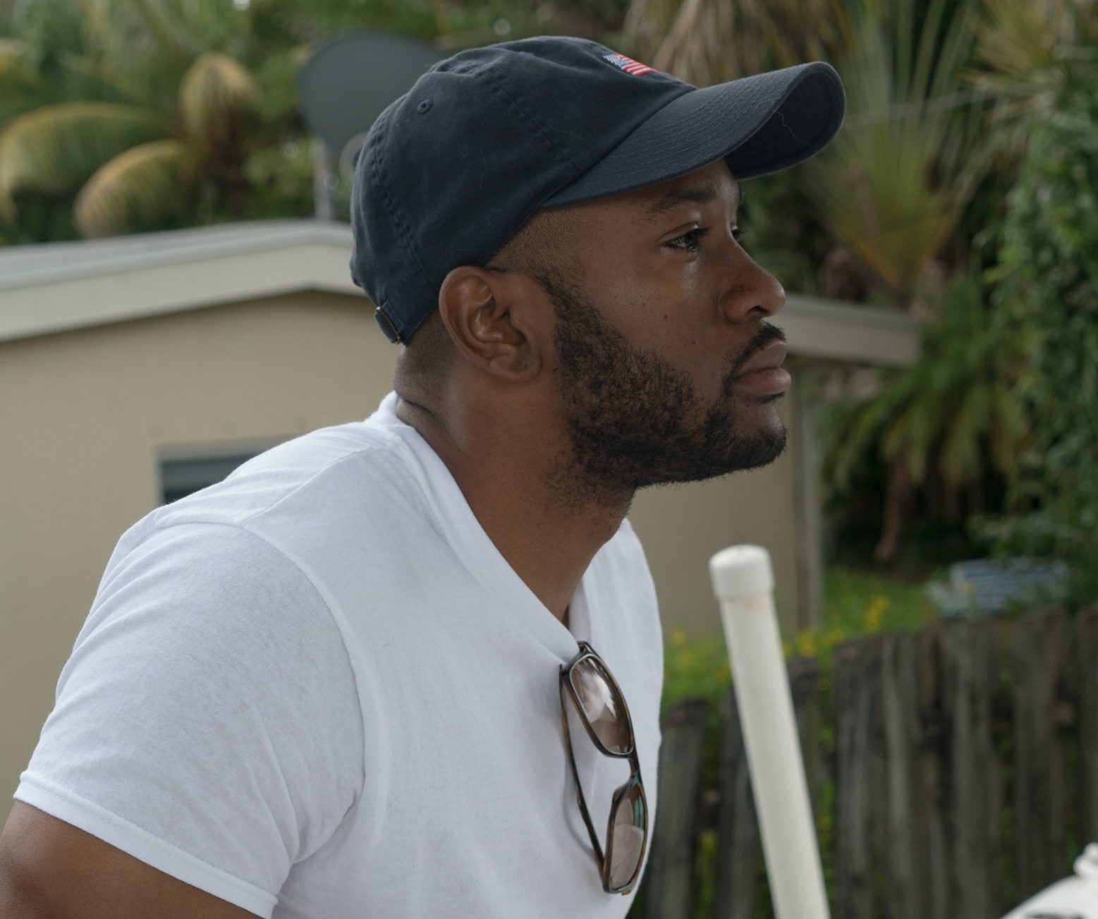 Carlos Burnell Miller outdoors in South Florida, in profile, wearing a dark cap and a white shirt.
